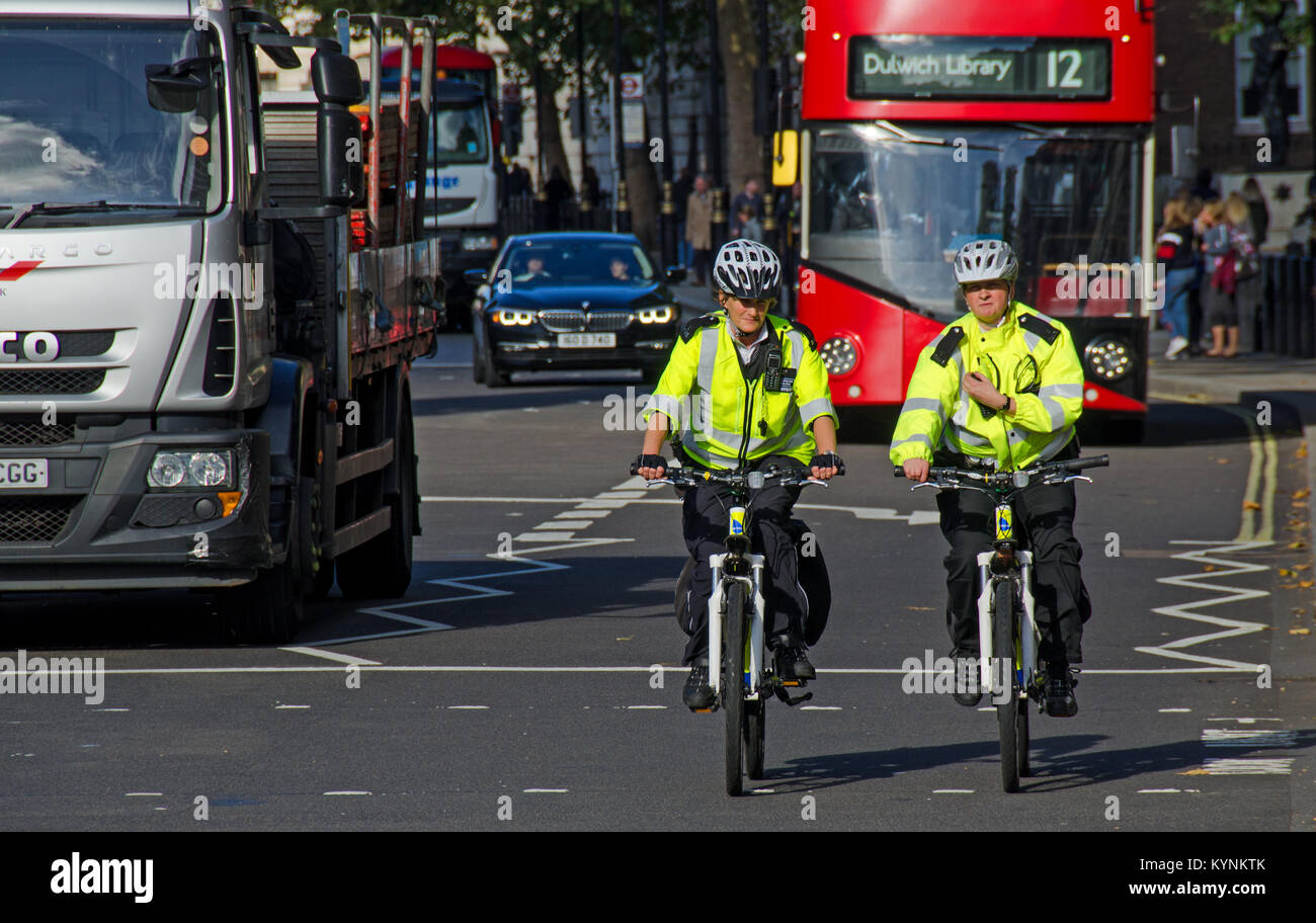 London, England, UK. Zwei weibliche Metropolitan Police bietet auf Fahrrädern vor einem roten Doppeldeckerbus Stockfoto