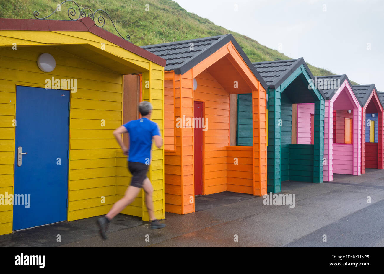 Jogger laufen an bunten Strandhütten am Saltburn Beach vorbei. Saltburn am Meer, North Yorkshire, England. VEREINIGTES KÖNIGREICH Stockfoto