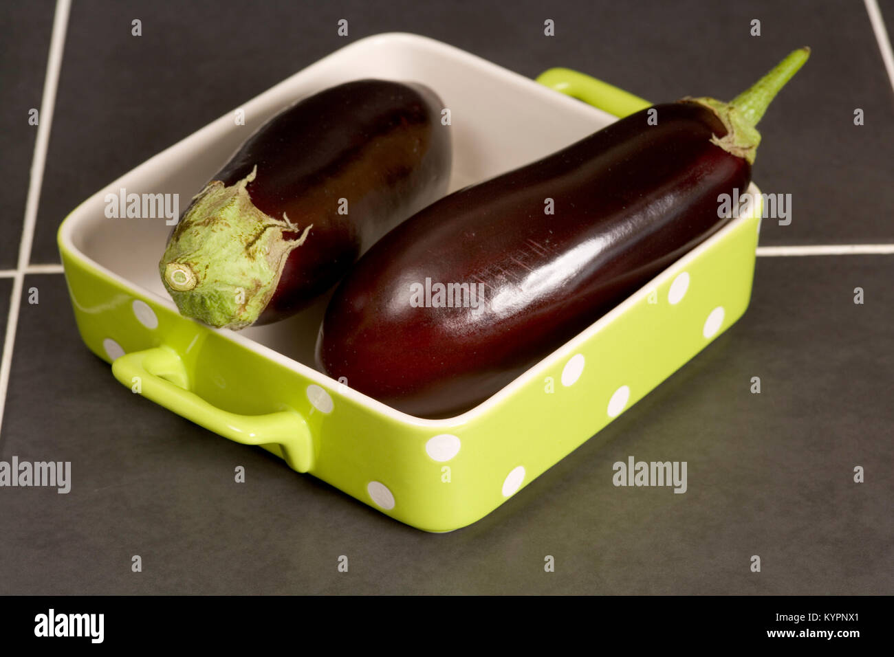 Zwei ganze rohe Auberginen in einem weiß gefleckte Lime Green Auflaufform Stockfoto