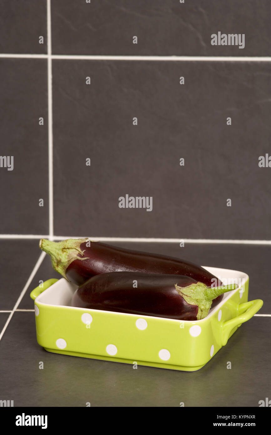 Zwei ganze rohe Auberginen in einem weiß gefleckte Lime Green Auflaufform Stockfoto