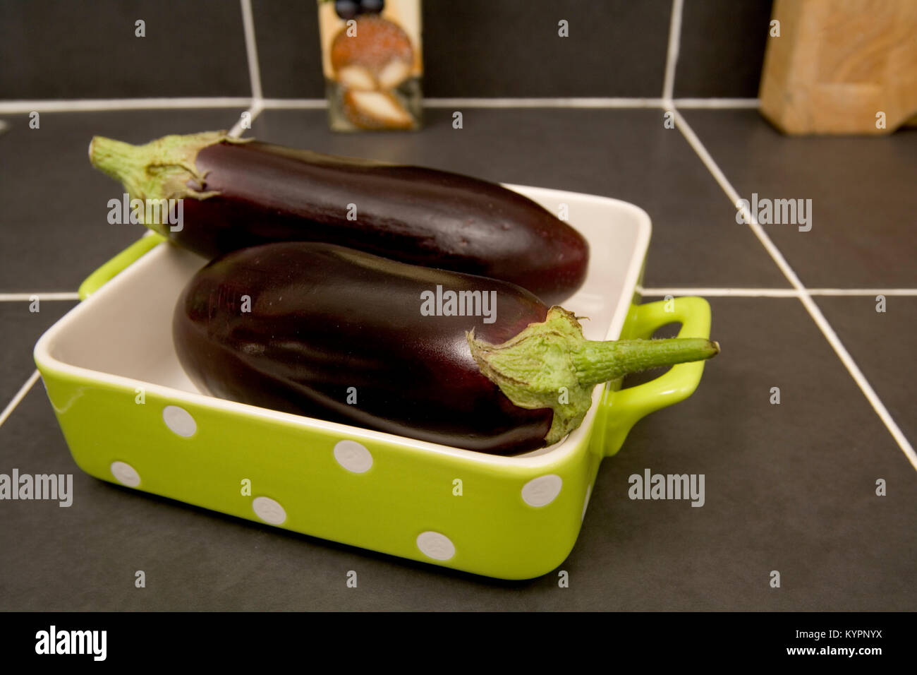 Zwei ganze rohe Auberginen in einem weiß gefleckte Lime Green Auflaufform Stockfoto