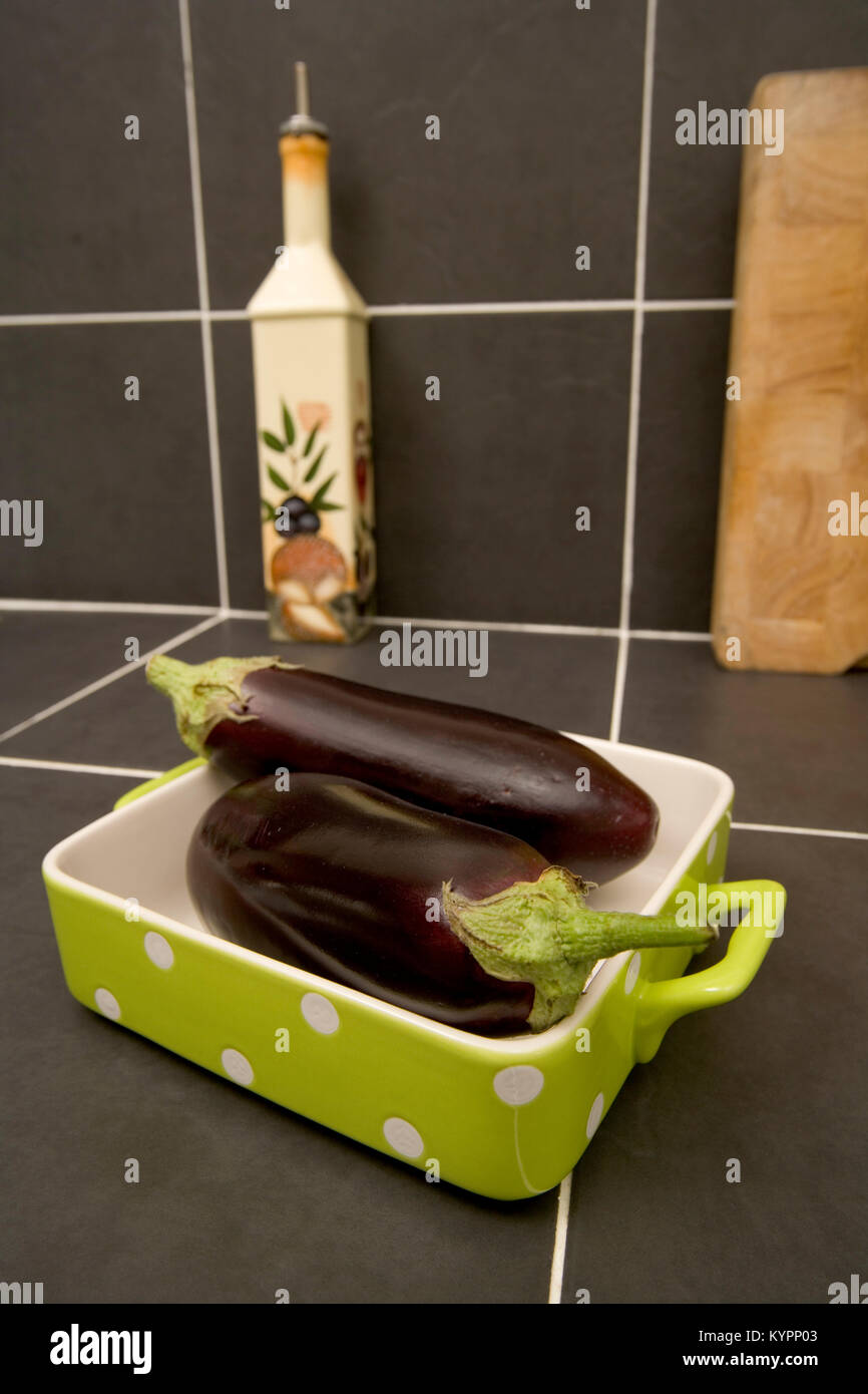 Zwei ganze rohe Auberginen in einem weiß gefleckte Lime Green Auflaufform Stockfoto