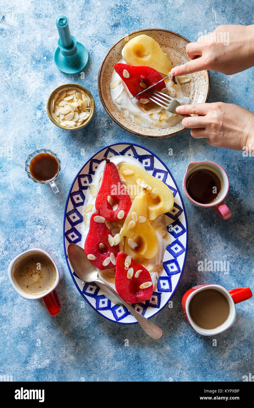 Pochierte Birnen serviert mit griechischem Joghurt, Ahornsirup und Mandelflocken Stockfoto
