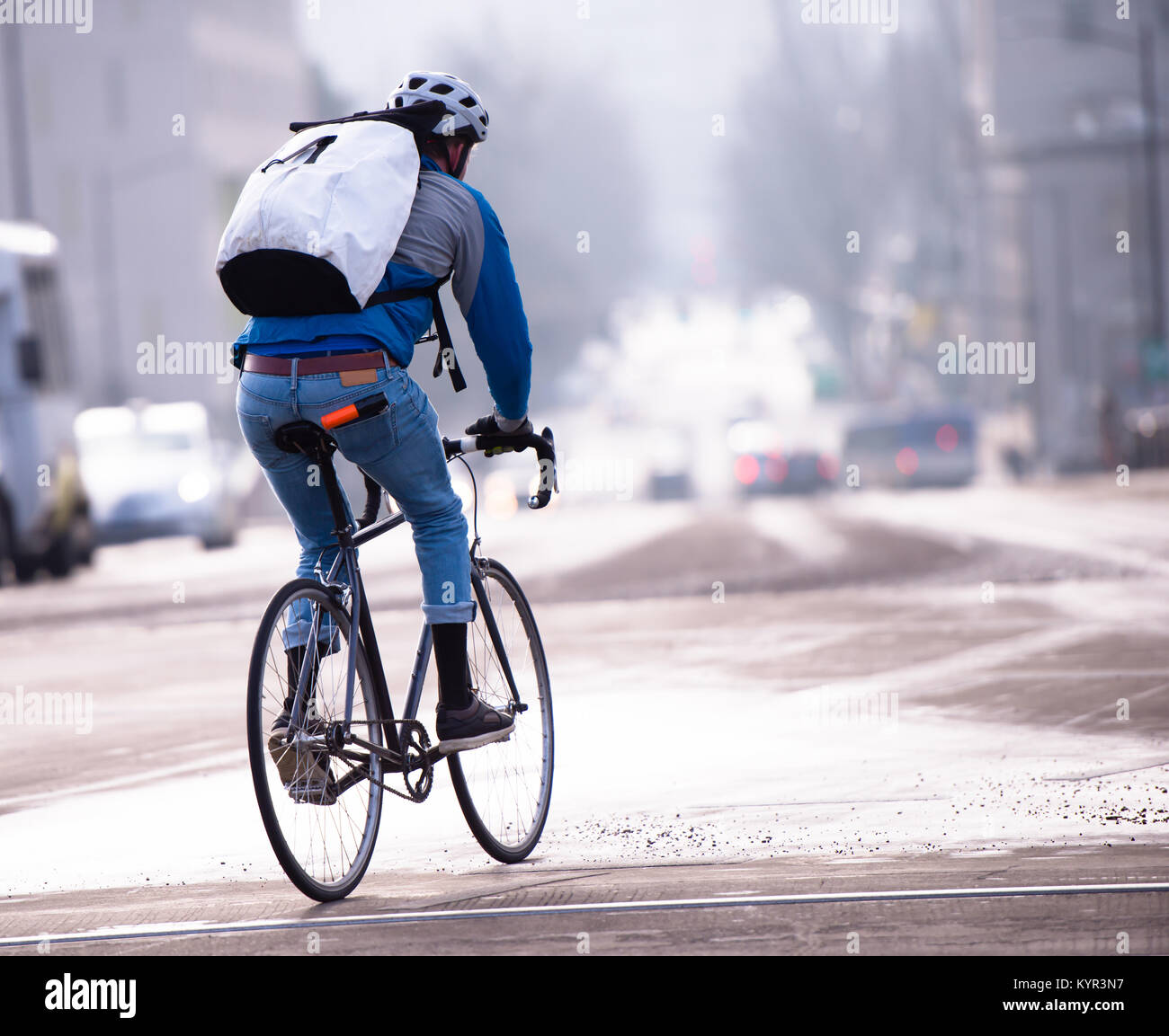 Ein Mann in Jeans und Turnschuhe in einem Schutzhelm und mit einem Rucksack  hinter den Schultern geniet, ein Rennrad durch die Straen von einem  modernen Stockfotografie - Alamy