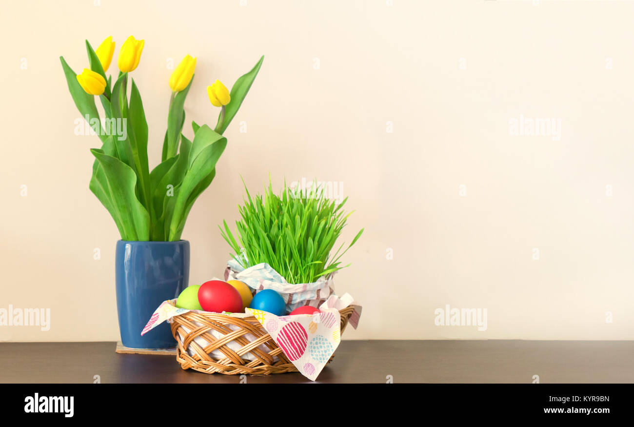 Einen Weidenkorb mit bunten Ostereiern, gelbe Tulpen in der Vase, Ostern Dekoration auf hellen Hintergrund. Freier Platz für Ihren Text. Stockfoto