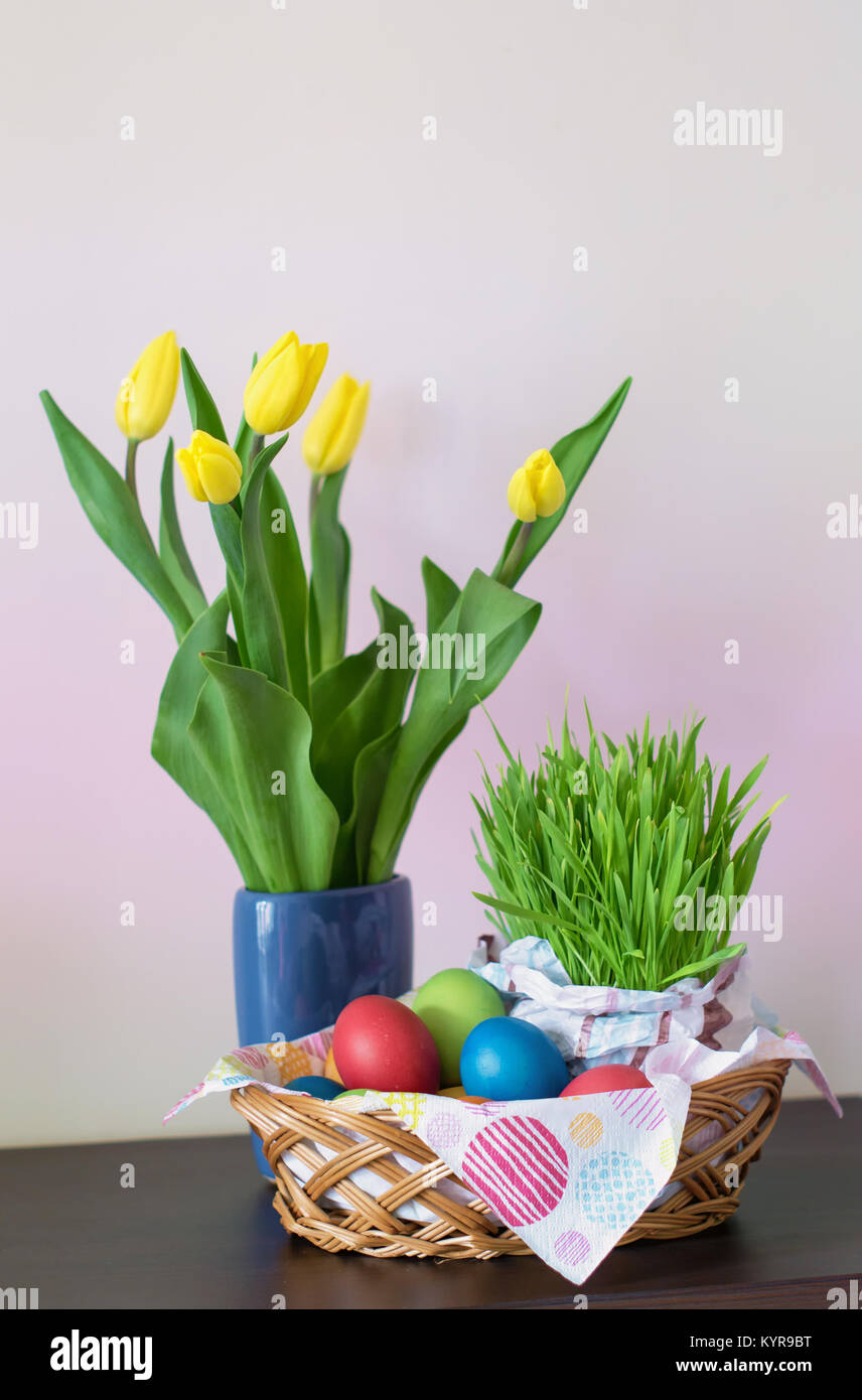Einen Weidenkorb mit bunten Ostereiern, gelbe Tulpen in der Vase, Ostern Dekoration auf hellen Hintergrund. Freier Platz für Ihren Text. Stockfoto