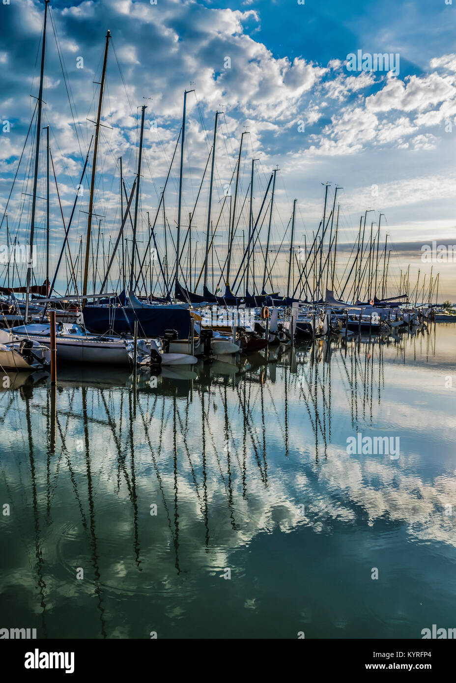 Ruhige See, Hafen und Pier bei Sonnenaufgang. Hafen mit Segelbooten und Pier in der Dämmerung mit dramatischen Wolken im Wasser spiegelt, Plattensee, Ungarn. Stockfoto