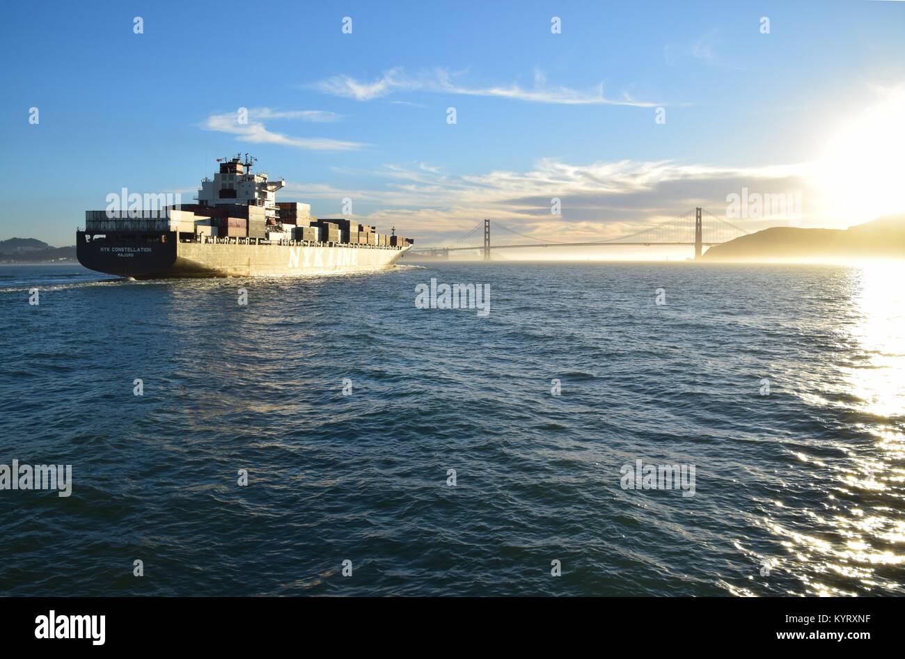 Containerschiff NYK Konstellation verläßt die Bucht von San Francisco unter der Golden Gate Bridge in den Sonnenuntergang. Stockfoto