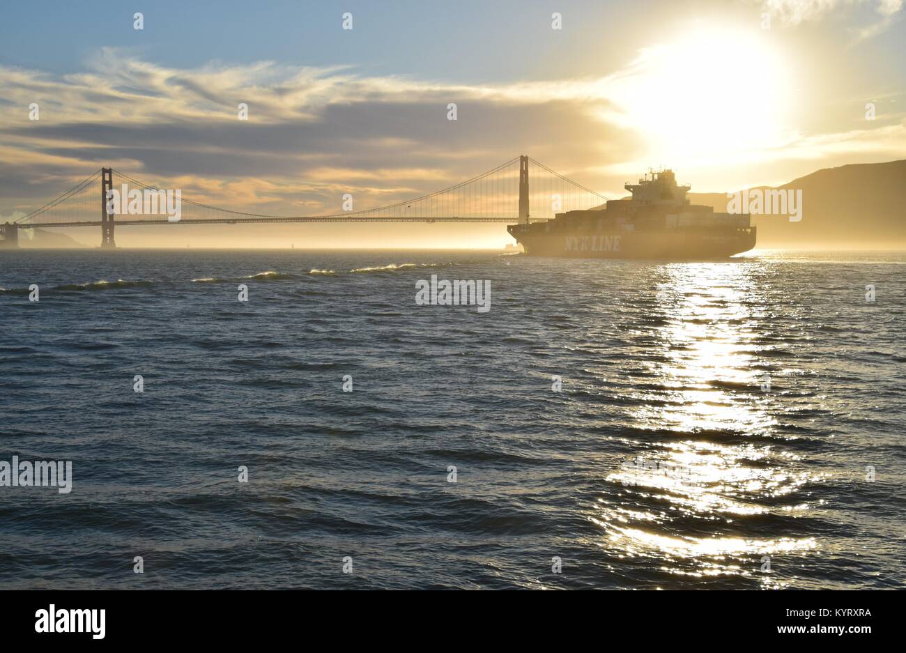 Containerschiff NYK Konstellation verläßt die Bucht von San Francisco unter der Golden Gate Bridge in den Sonnenuntergang. Stockfoto