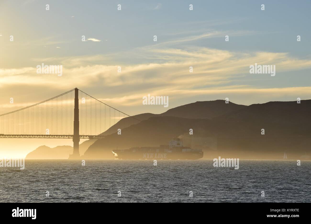 Containerschiff NYK Konstellation verläßt die Bucht von San Francisco unter der Golden Gate Bridge in den Sonnenuntergang. Stockfoto