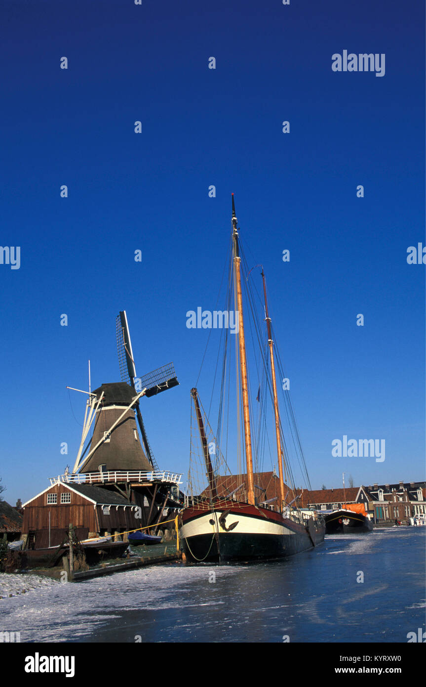 Die Niederlande. Woudsend. Winter. Eislaufen. Schlitten. Windmühle. Saling Boot in gefrorenen Kanal. Stockfoto