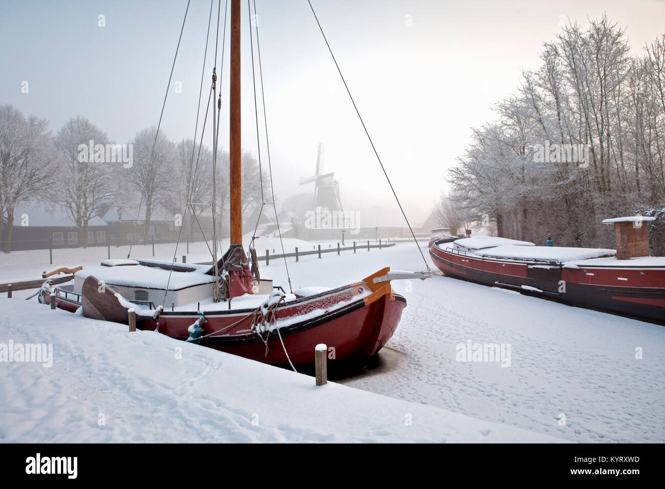 Die Niederlande, Sloten, Traditionelle segeln Frachtschiff in gefrorenen Kanal. Hintergrund Windmühle. Stockfoto