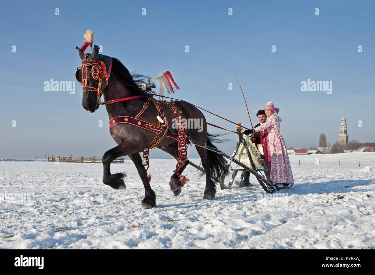 Die Niederlande, Hindeloopen, Antike mit Pferd und Schlitten und Friesenpferd. Mann und Frau in traditioneller Tracht. Winter. Stockfoto