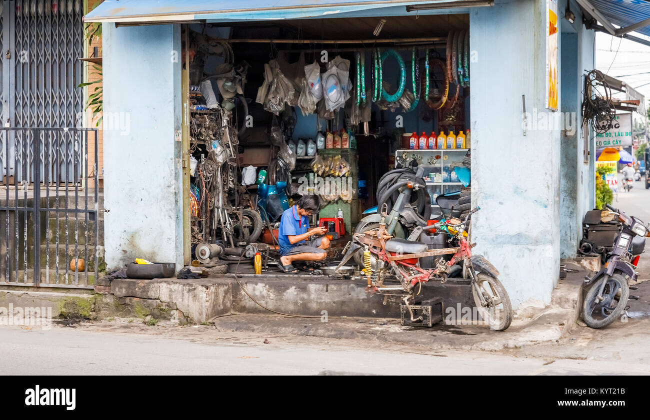 Blick auf die Straße in einem Vorort von Saigon (Ho Chi Minh City), South Vietnam: lokalen vietnamesischen Mann in eine offene Fassade am Straßenrand Motorrad Werkstatt arbeiten Stockfoto