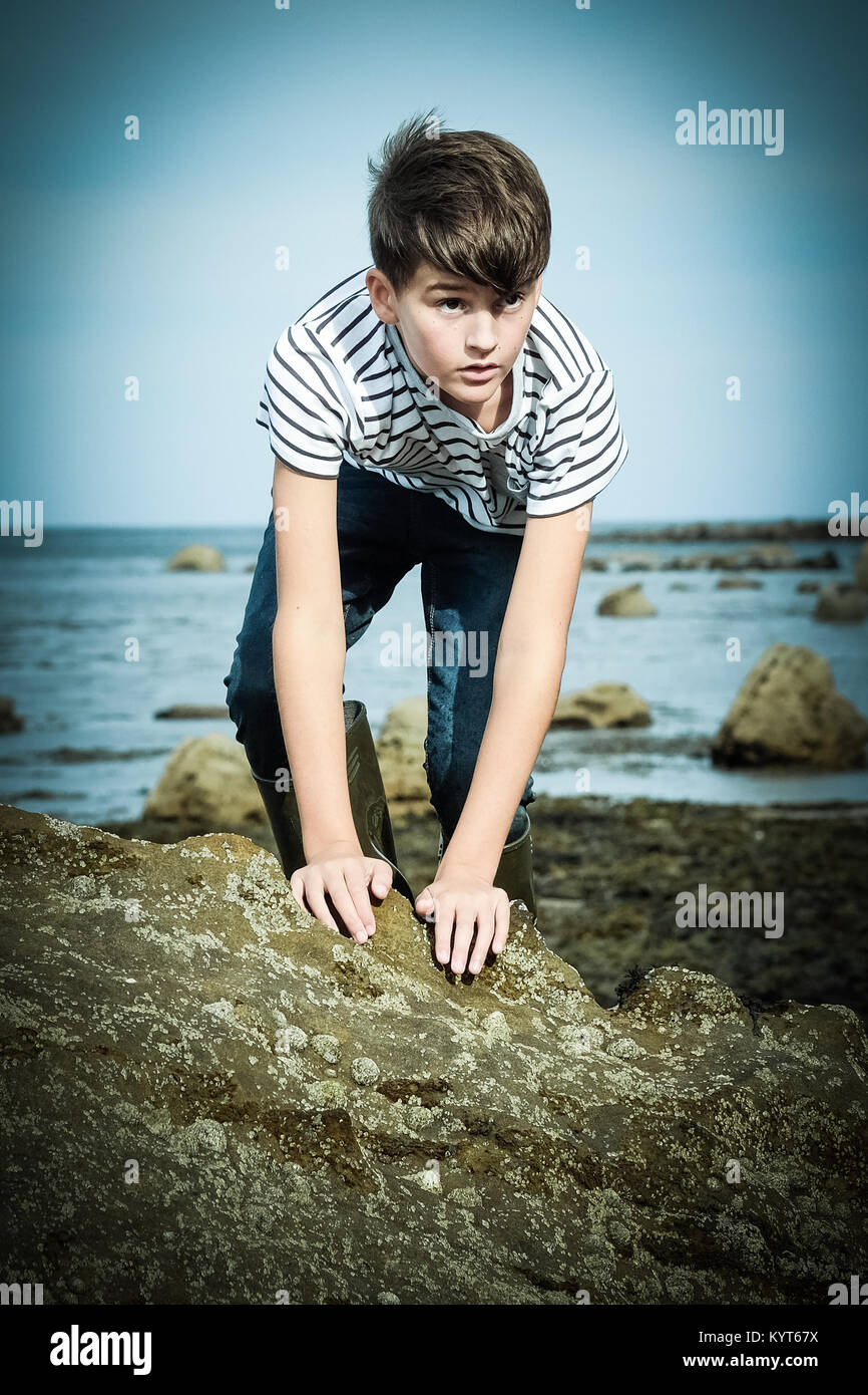 10 Jahre alter Junge Klettern am Felsen im Meer bei [Songbook] Bay, Yorkshire, Großbritannien Stockfoto