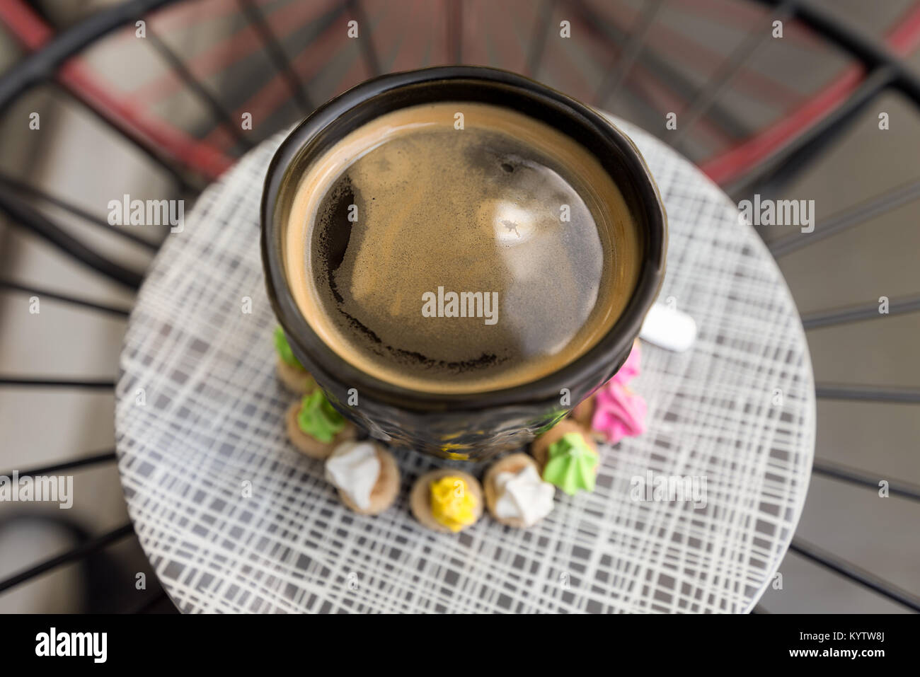 Hot Americano Kaffee mit Crema top in stilvollem Schwarz Glas umgeben farbenfrohe classic Ice Gem Süßigkeiten Kekse auf einem gemusterten Platte kaufen. Stockfoto