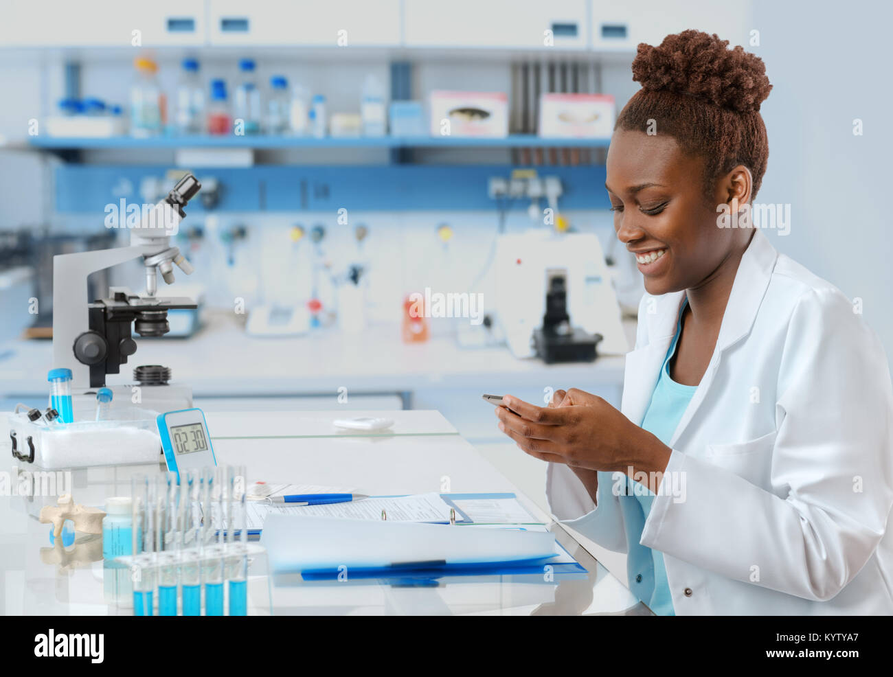 Afrikanisch-amerikanische Biologe im Labor jemand Textnachrichten auf Ihr Mobiltelefon mit einem Lächeln Stockfoto