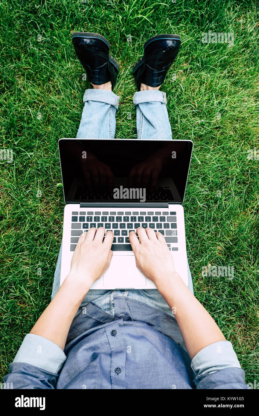 7/8 Schuß von Mann mit Laptop mit leerer Bildschirm während der Sitzung auf grünem Gras Stockfoto