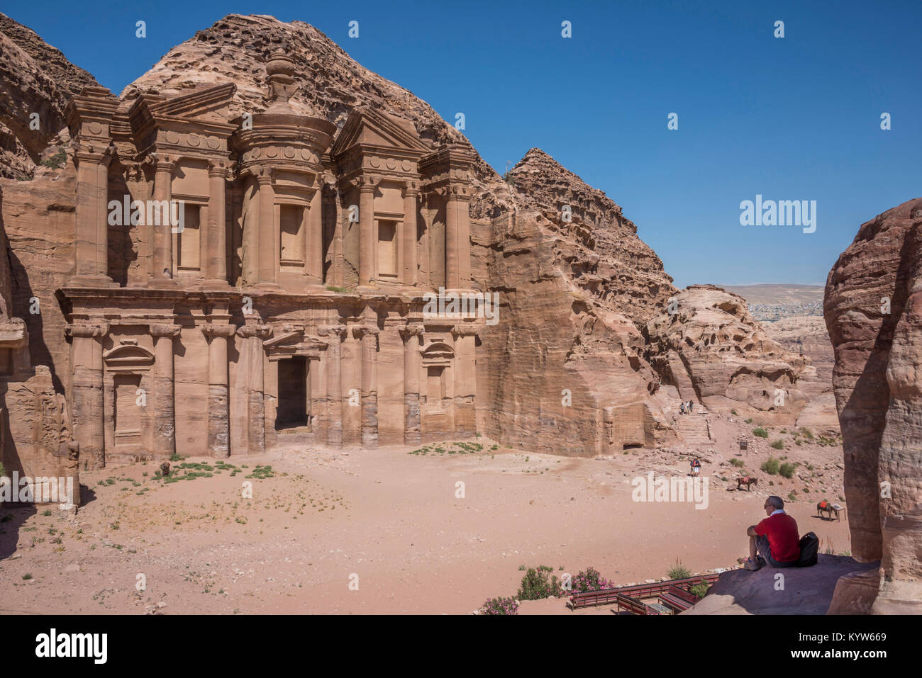 Ein Tourist im Schatten eines Felsen sitzt, beobachtet das Kloster der Stadt Petra in Jordanien Stockfoto