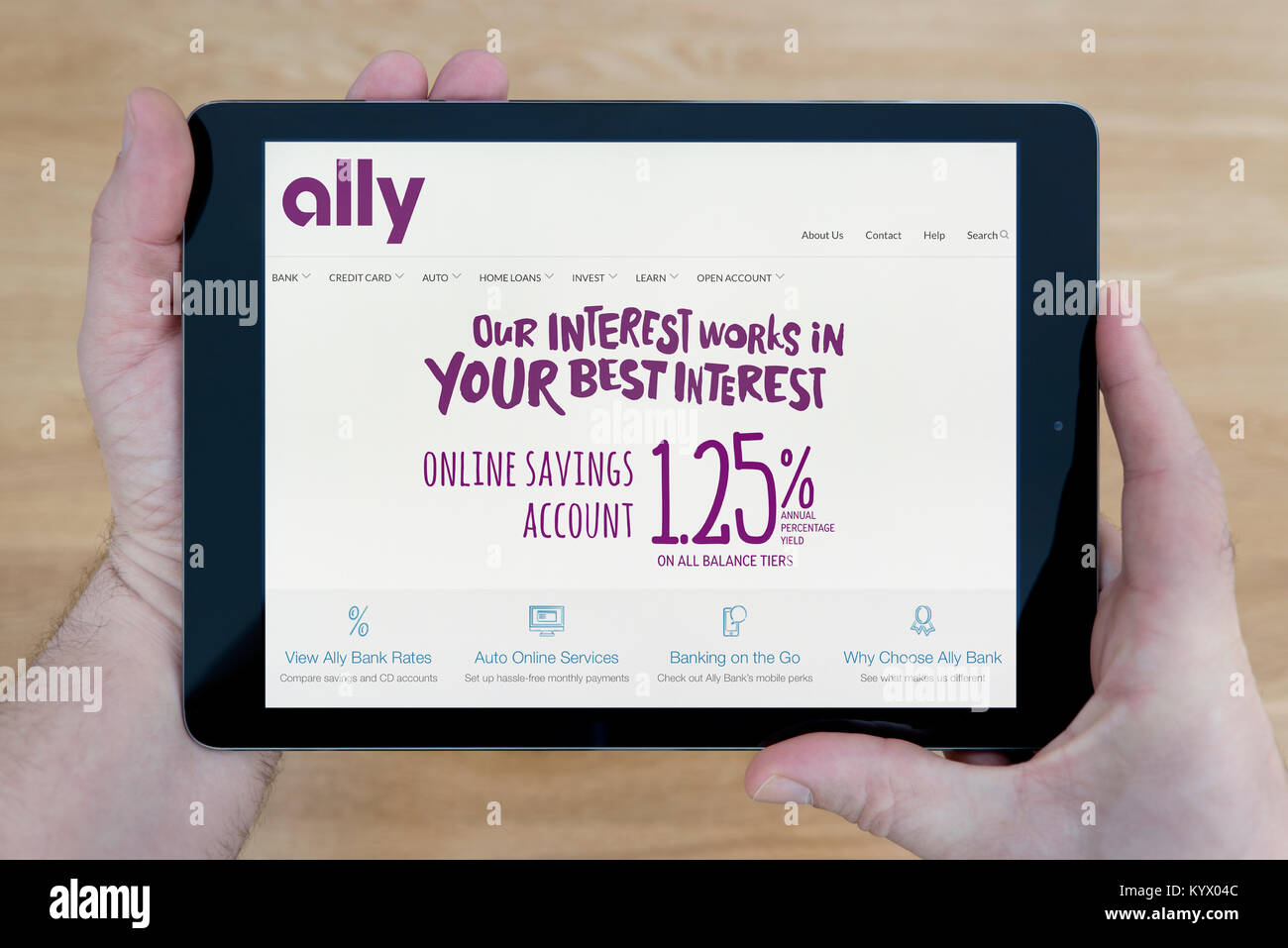 Ein Mann sieht bei der Ally Bank Website auf seinem iPad tablet device, mit einem hölzernen Tischplatte Hintergrund (nur redaktionelle Nutzung) Stockfoto