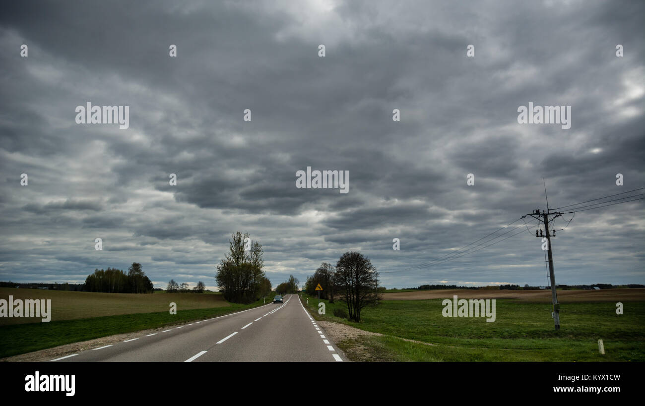 Asphaltierte Straße mit dem Auto weit weg an bewölkten Frühling mit Strommast in Litauen. Stockfoto