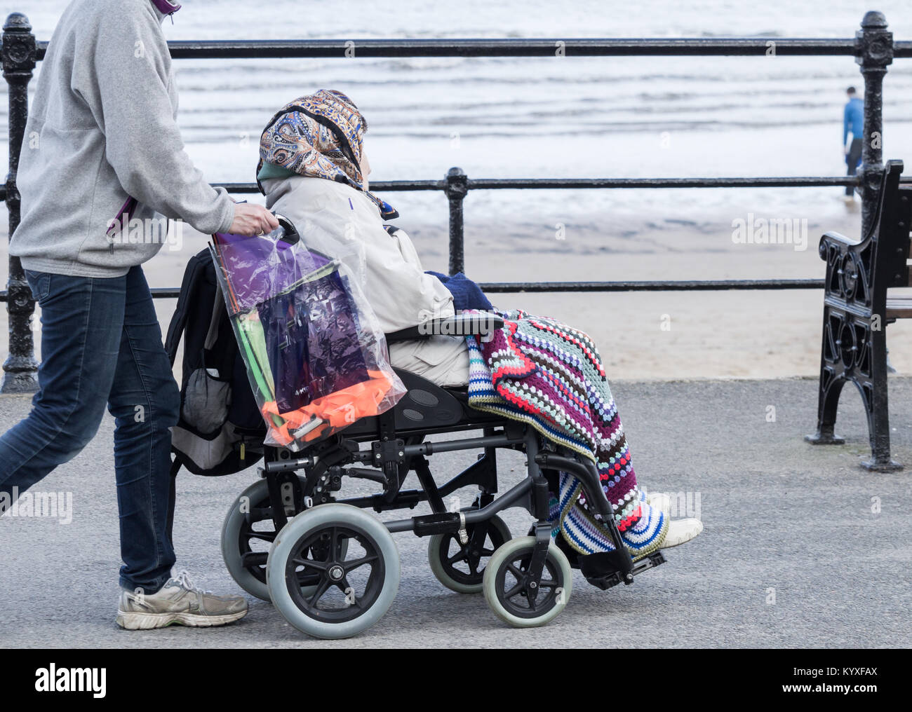 Jüngere Person (Pflege/Familie?) Rollstuhl schieben mit älteren Frau entlang der Küste. Großbritannien Stockfoto