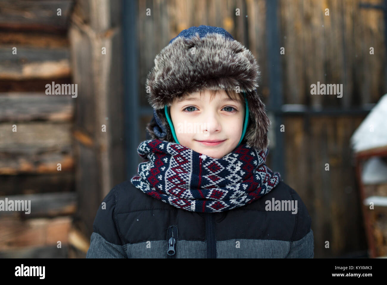 Schöne Kind mit einem sanften Lächeln in warme Kleidung gegen Holz- Hintergrund. Junge gekleidet im Winter warm. Stockfoto