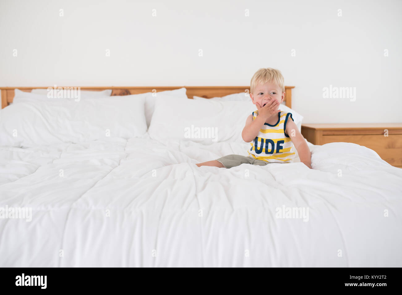 Junge mit Hand, Mund, beim Sitzen auf dem Bett Stockfoto