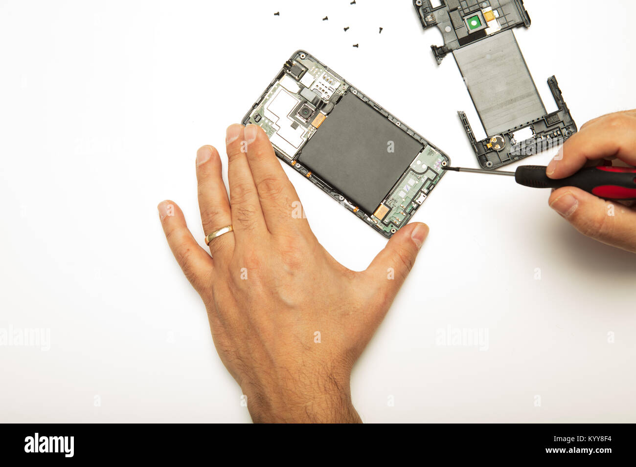 Mann tun, Anpassungen und Reparaturen auf sein Smartphone mit einem Präzisions Schraubendreher in der Nähe zu sehen, der seine Hände und die demontierten Mobiltelefon auf Stockfoto