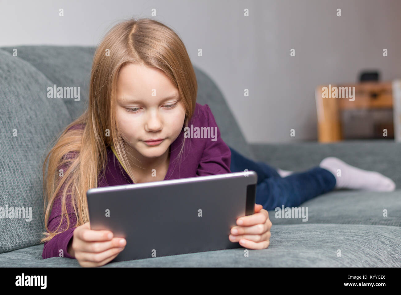 Ein Mädchen liegt auf dem Sofa mit einem Tablet-PC im Wohnzimmer Stockfoto