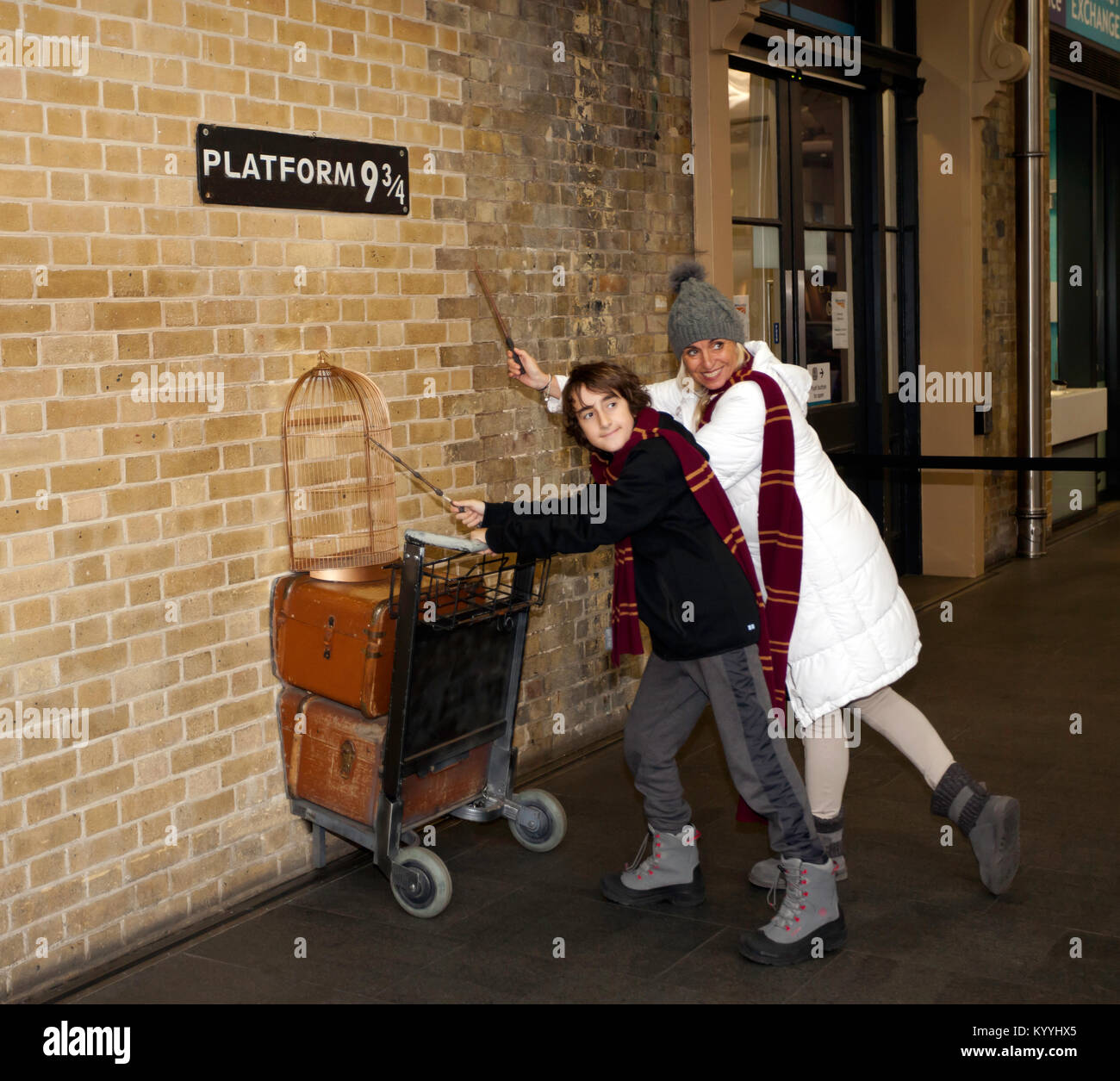 Harry Potter Fans pose mit Zauberstäbe und Gryffindor Schals durch eine Replik der Katze in Plattform 9 3/4 im Bahnhof Kings Cross, London Stockfoto