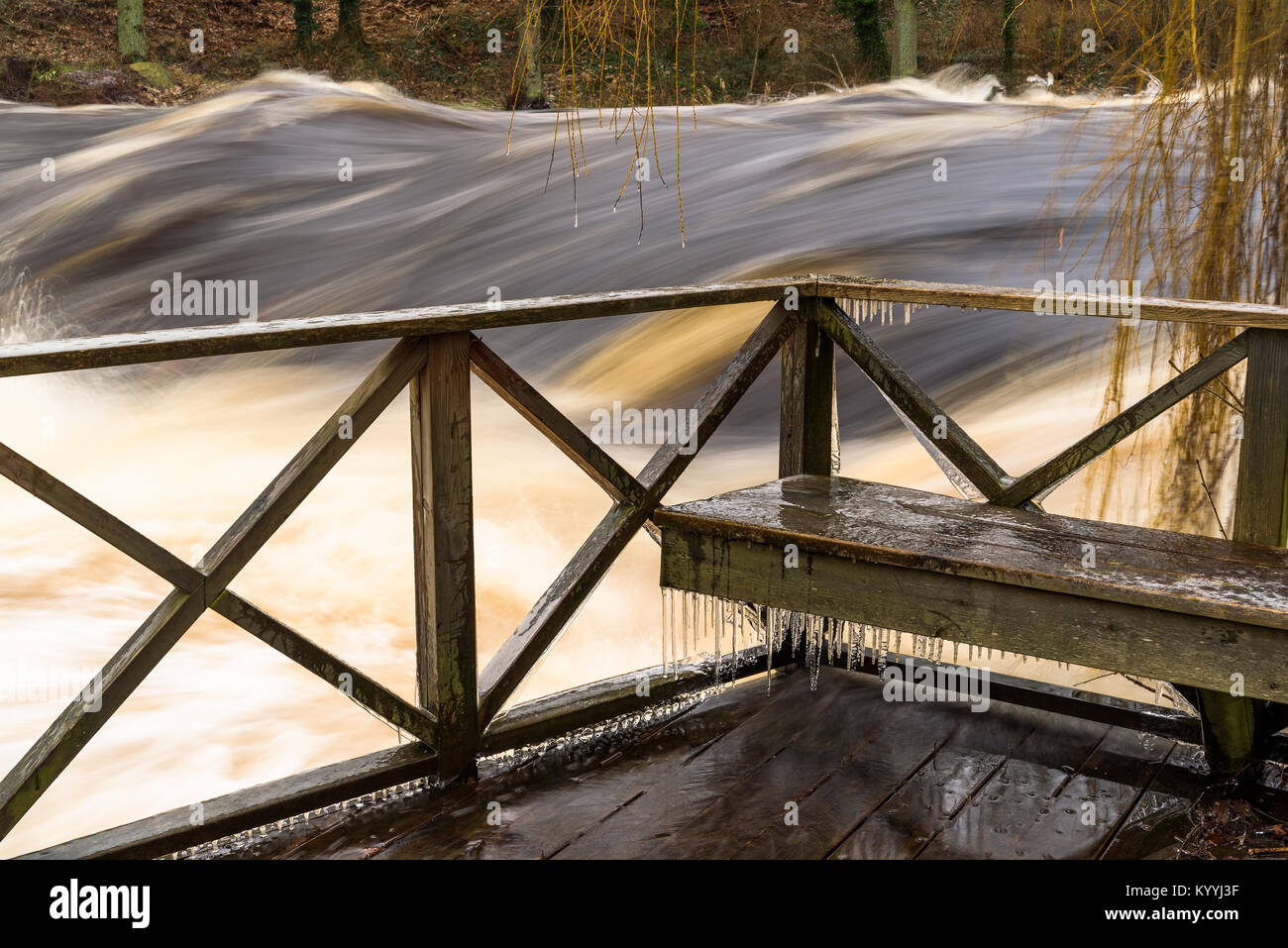 Holzbank am Balkon mit Blick auf einen reissenden Fluss. Eiszapfen bilden auf der Bank in dem kalten Wetter. Stockfoto