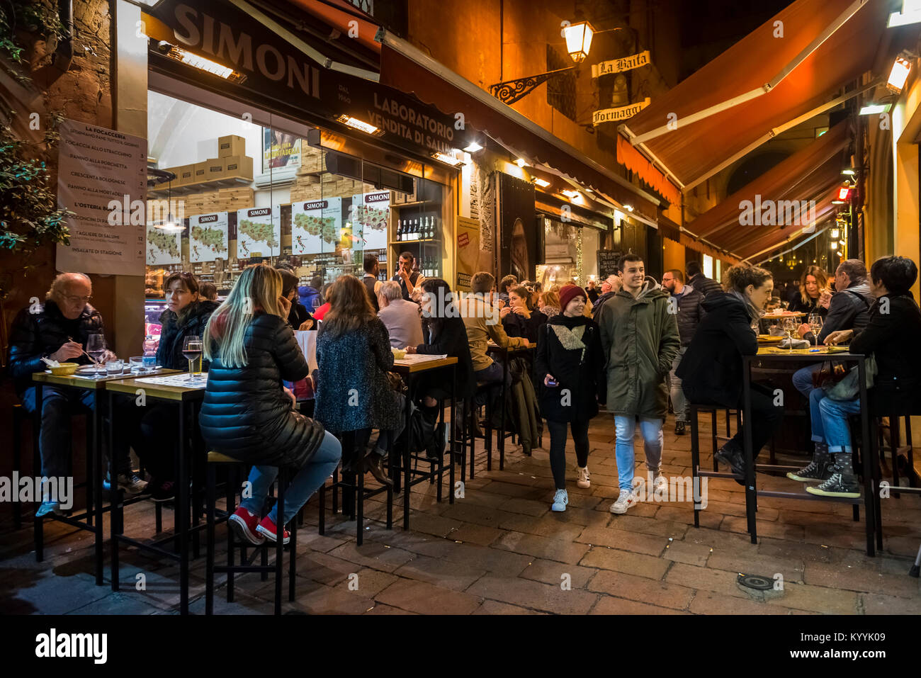 Die Menschen sitzen, essen und trinken in Restaurants, Cafés und Bars in der Via Pescherie Vecchie, eine Straße in der Stadt Bologna, Italien bei Nacht Stockfoto