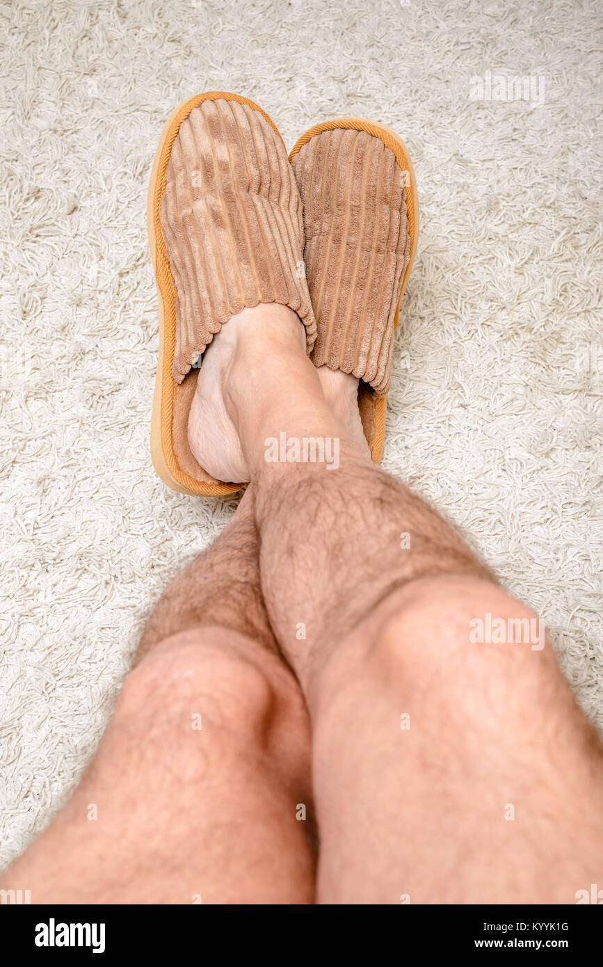Ein Mann mit behaarten Beinen trägt warme Hausschuhe und Entspannen mit den Füßen auf einem wollteppich Stockfoto