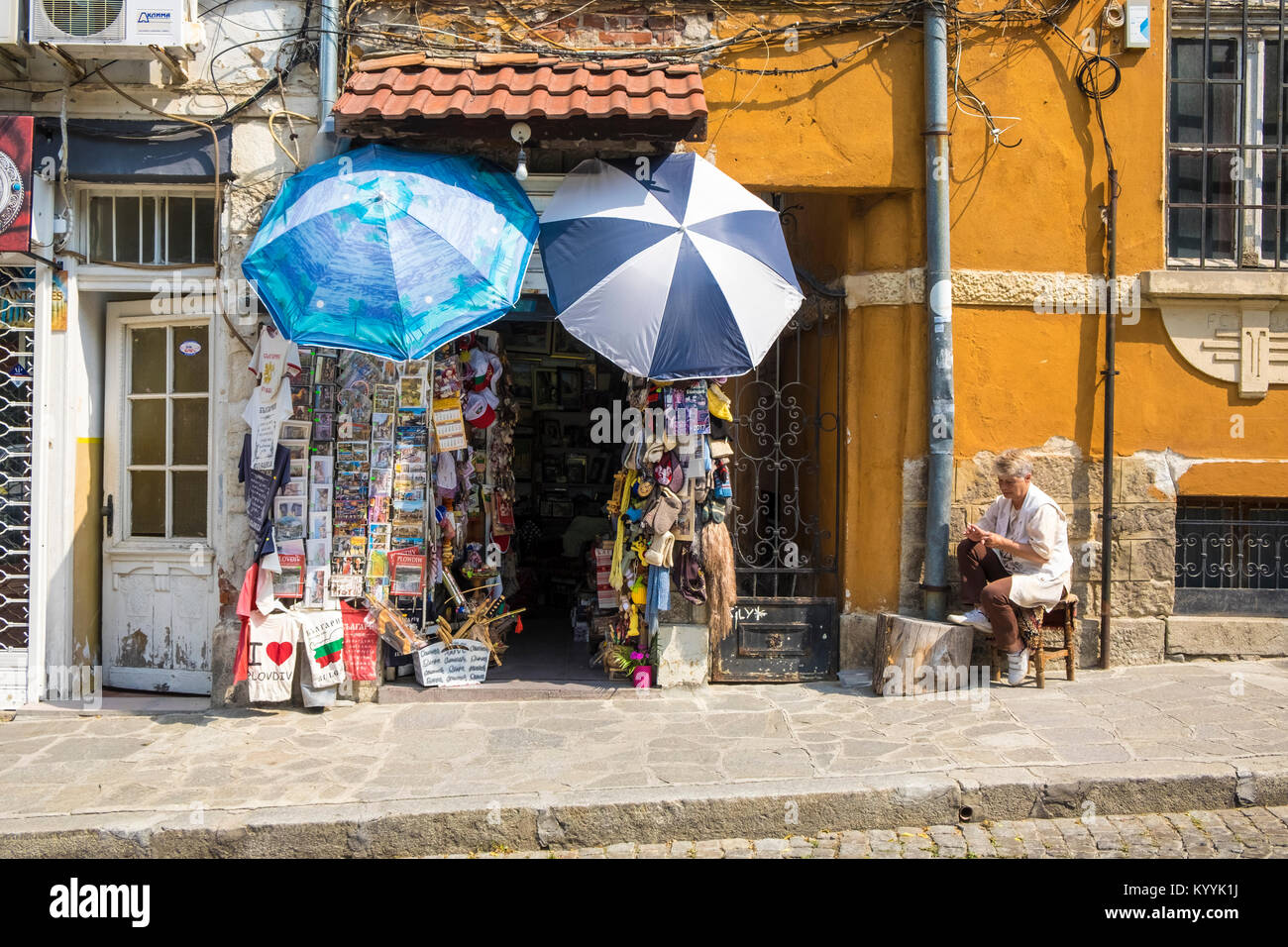 Ladenbesitzer vor dem Eingang zu Ihrem kleinen, alten Souvenir shop in Plovdiv, Bulgarien, Europa sitzen Stockfoto