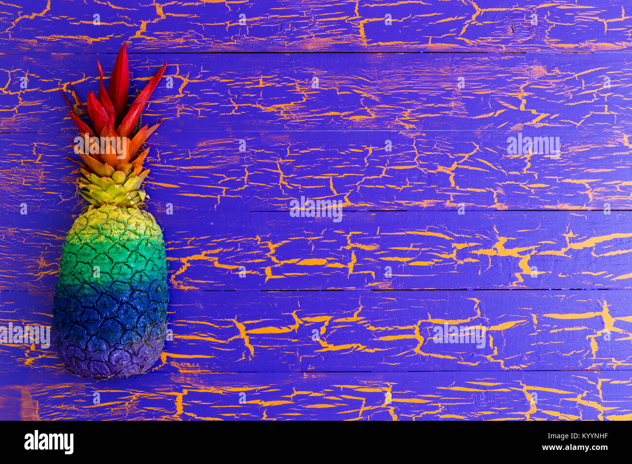 Bunte Ananas in Regenbogenfarben, die eine Seite der Grenze auf einer hölzernen Hintergrund mit Gecrackten blaue Farbe und Textur kopieren Raum Stockfoto