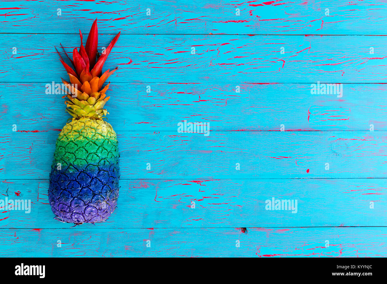 Hoher winkel Nahaufnahme eines ganzen Ananas in Streifen der lebendige Farben auf einem rustikalen Holztisch blau lackiert Stockfoto
