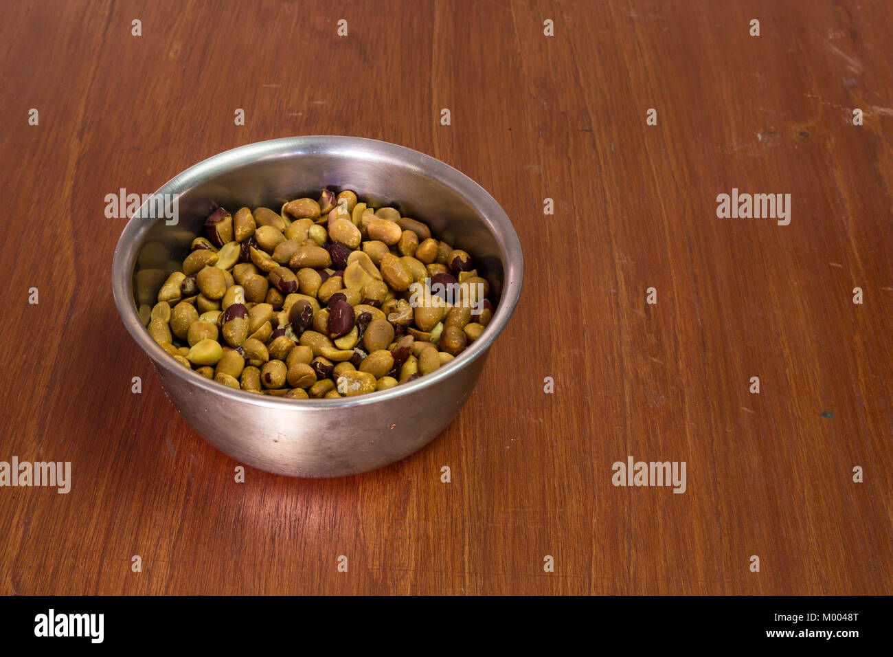 Hausgemachte geröstete Erdnüsse in Edelstahl Schüssel, Mitte links, auf hölzernen Tisch Stockfoto