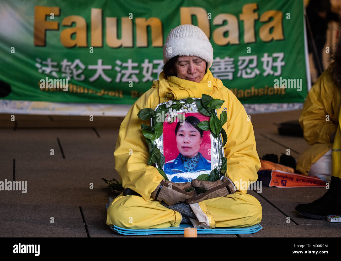 Frankfurt am Main, Deutschland. 13 Jan, 2018. Ein Anhänger der Glaubensgemeinschaft Falun Dafa (auch Falun Gong) sitzt mit einem Foto von einem möglichen Opfer von Folter der religiösen Bewegung an der shoppin street Zeil in Frankfurt am Main, Deutschland, 13. Januar 2018. Falun Gong 1992 in China entwickelt. Seitdem ist sie auf der ganzen Welt. Falun Gong wurde vor allem im Westen durch das Verbot im Jahr 1999 bekannt, und die staatliche Verfolgung. Credit: Andreas Arnold/dpa/Alamy leben Nachrichten Stockfoto