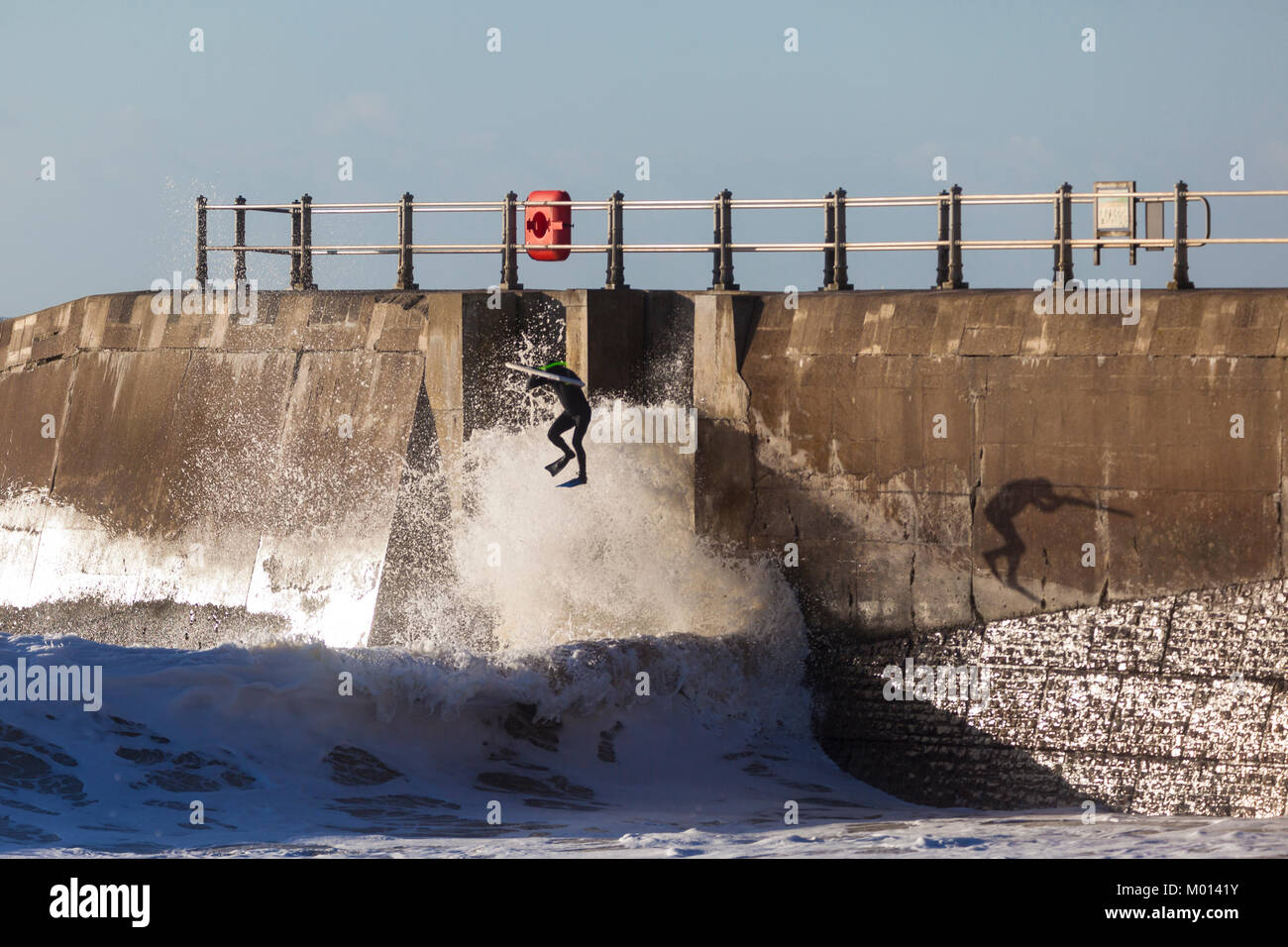 Hastings, East Sussex, UK. 18. Januar, 2018. Die Sonne scheint, aber es ist sehr windig hier in Hastings, das Meer tobt Trotz der Ebbe zu werden, diese Surfer nutzen Sie die raue See über die hafenmauer wie es schafft größere Wellen, wie sie an die Küste kommen. Foto: Paul Lawrenson/Alamy leben Nachrichten Stockfoto