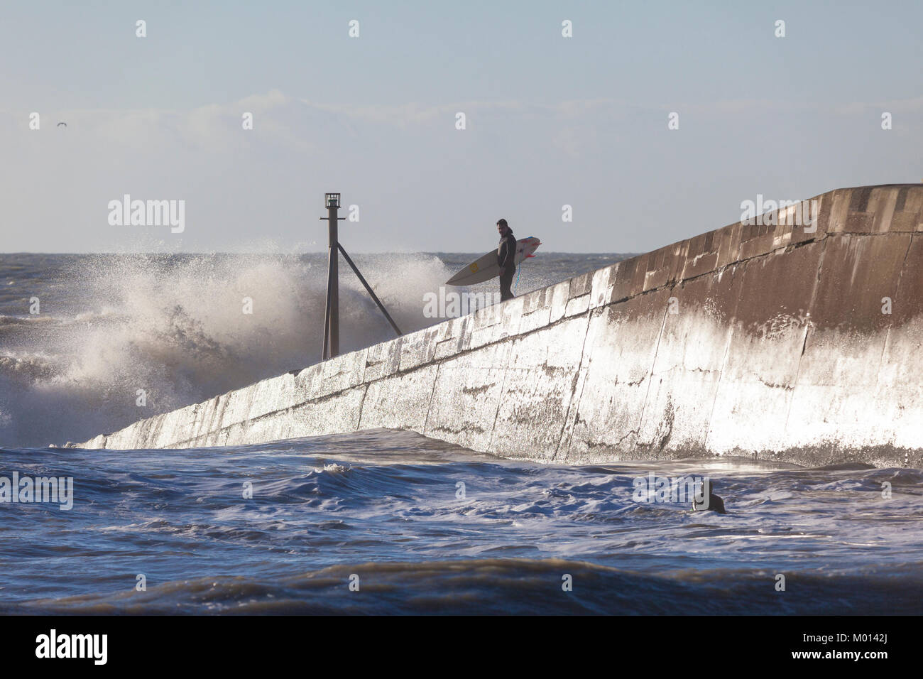 Hastings, East Sussex, UK. 18. Januar, 2018. Die Sonne scheint, aber es ist sehr windig hier in Hastings, das Meer tobt Trotz der Ebbe zu werden, diese Surfer nutzen Sie die raue See über die hafenmauer wie es schafft größere Wellen, wie sie an die Küste kommen. Wellen. Foto: Paul Lawrenson/Alamy leben Nachrichten Stockfoto