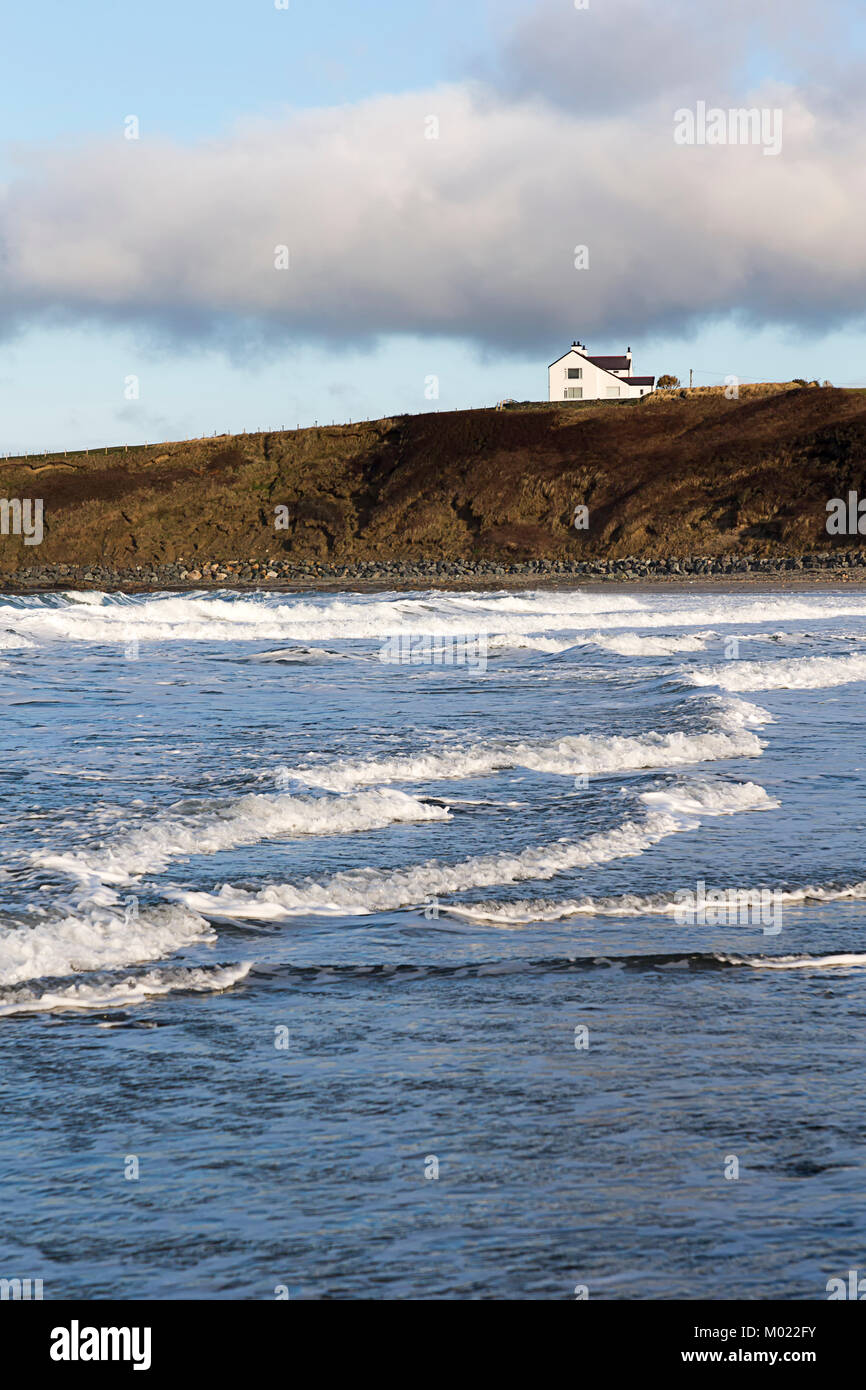 Blick auf ein weißes Haus auf den Klippen am Ende der Sandstrand, Porth Tywyn Mawr, Llanfwrog, Anglesey, über dem einströmenden Wasser Stockfoto