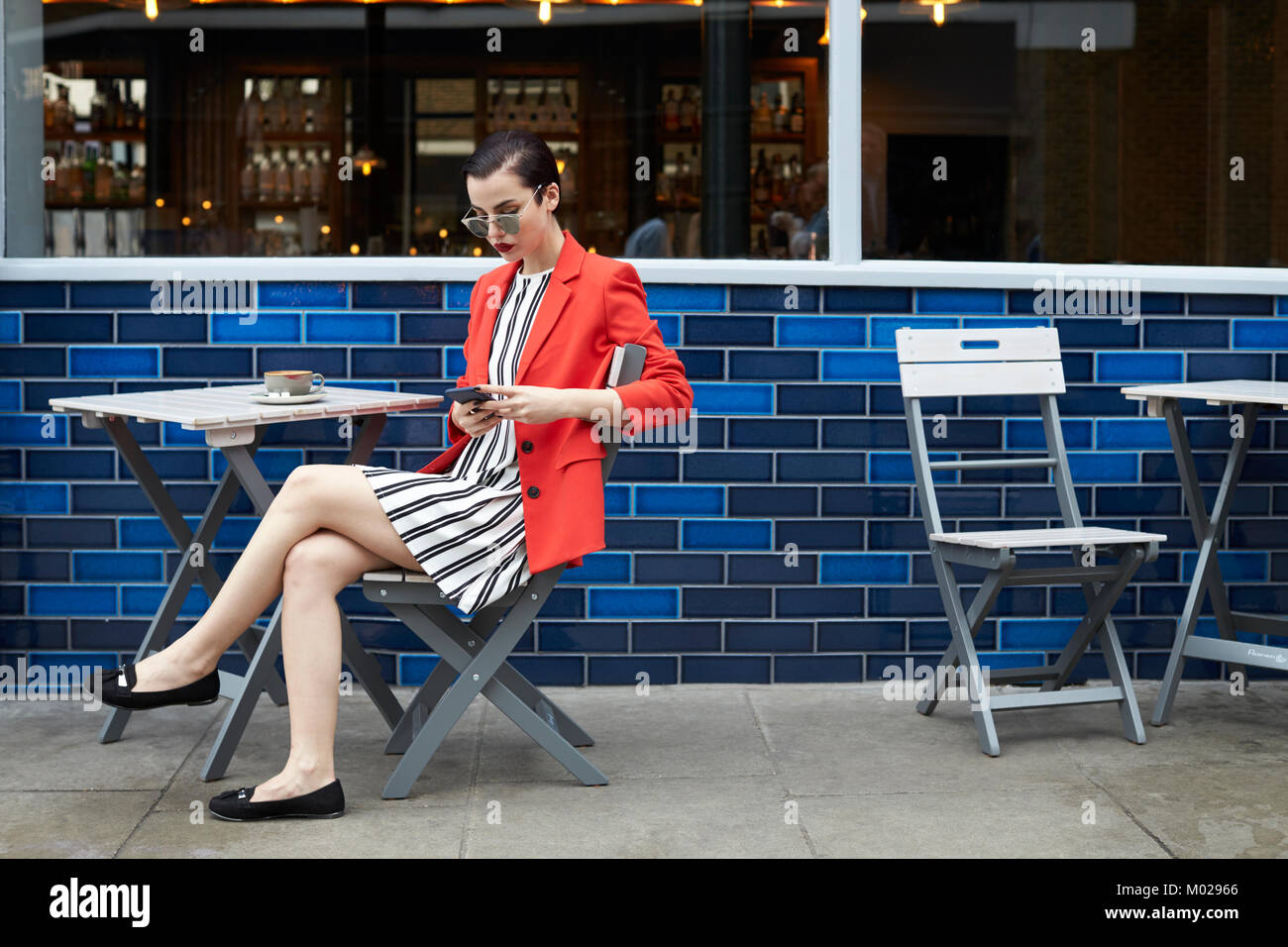 Frau vor einem Cafe mit Smartphone sitzen, Seitenansicht Stockfoto