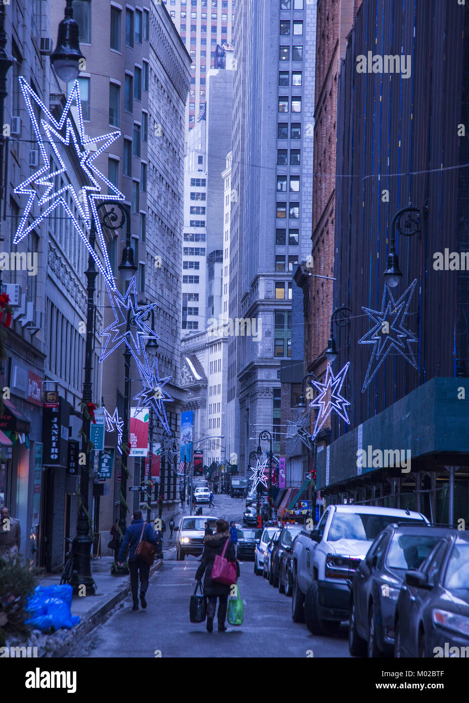 Nach unten schauen. Der schmale Nassau Street mit festlichen Dekorationen während der Weihnachtszeit in Lower Manhattan gesäumt. New York Stock Exchange peaks thr Stockfoto