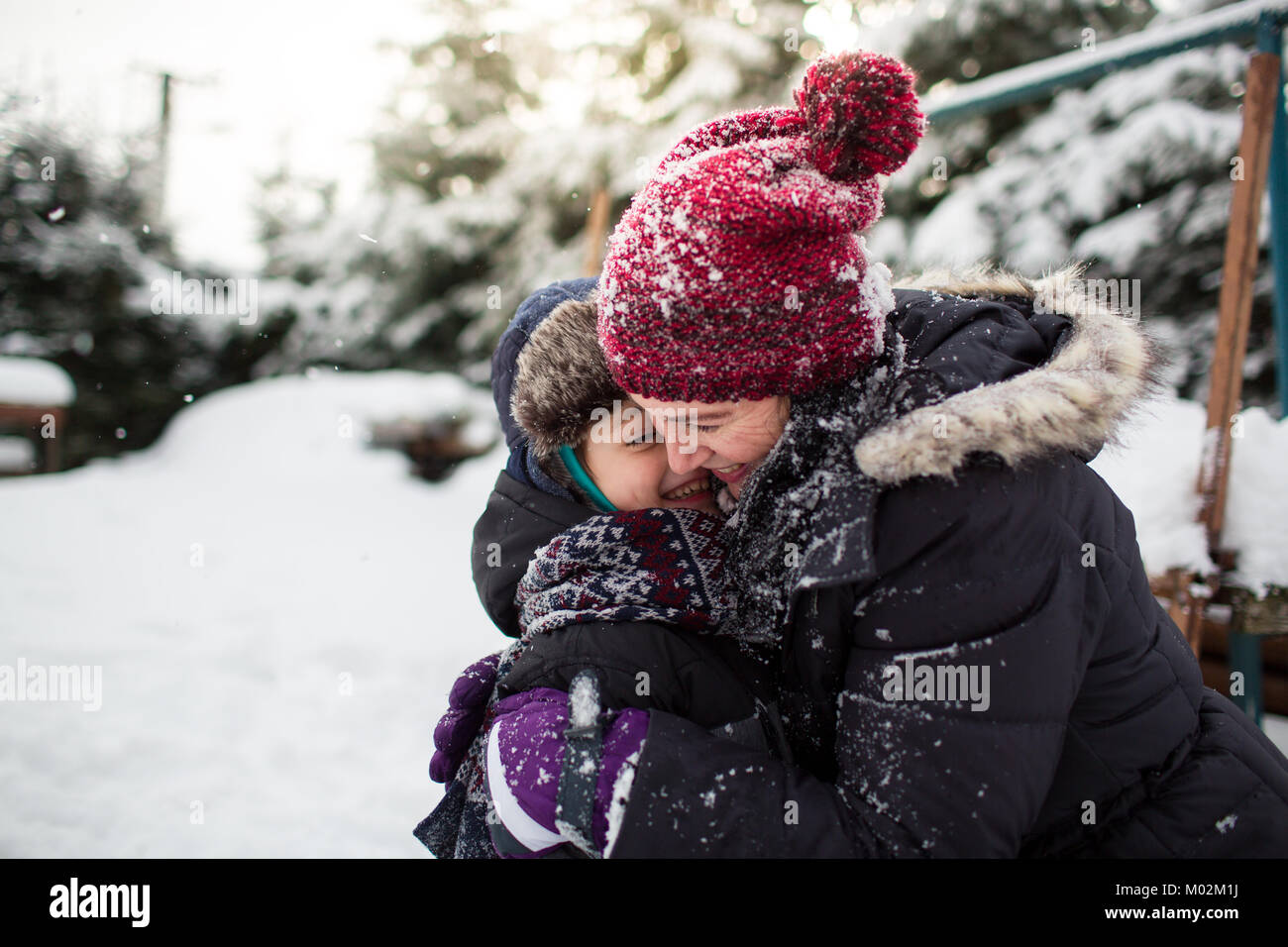 Seitliche Sicht auf eine glückliche Mutter und Sohn umarmen nach einer Schneeballschlacht. Familie Spaß im Schnee. Stockfoto