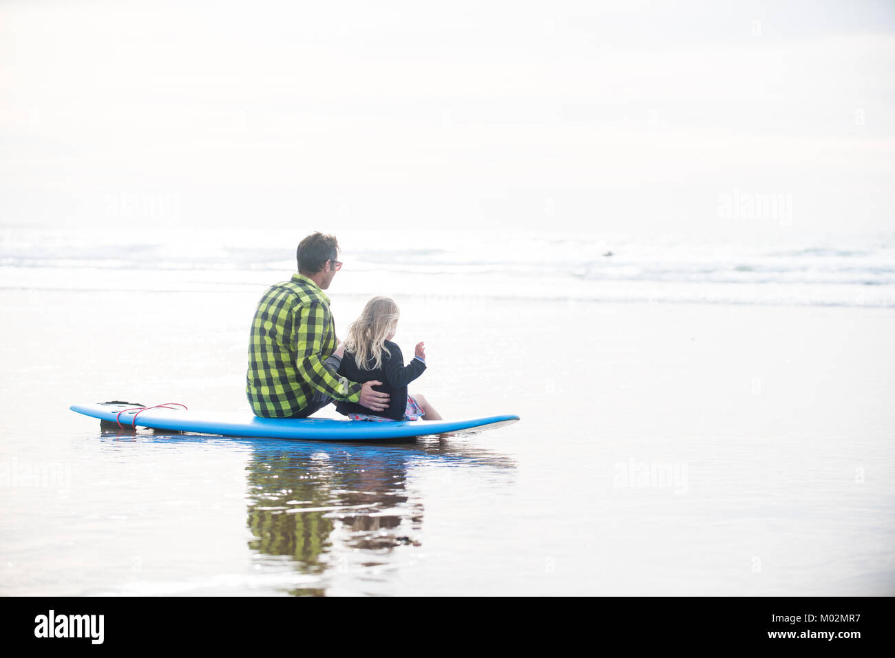 Ein Vater und eine Tochter saß auf einem sufboard auf die Wellen auf der Suche Stockfoto