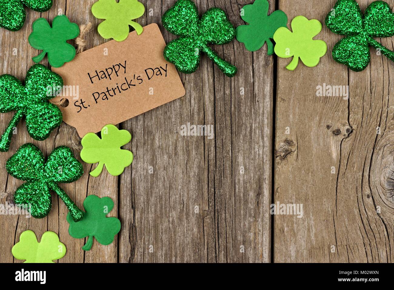 Happy St Patricks Day tag mit Ecke Grenze der glänzenden Shamrocks über eine rustikale Holz Hintergrund Stockfoto