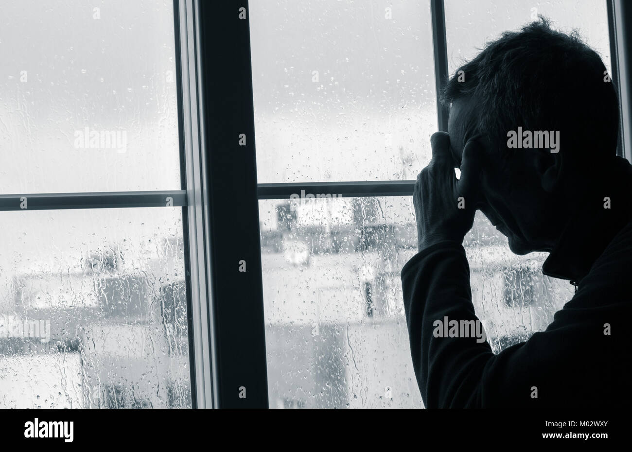 Reifer Mann mit der Hand auf den Kopf in der Nähe der Fenster an einem regnerischen Tag. Konzept Bild für Depressionen, männlichen Depression, psychische Gesundheit, männliche Selbstmord... Stockfoto