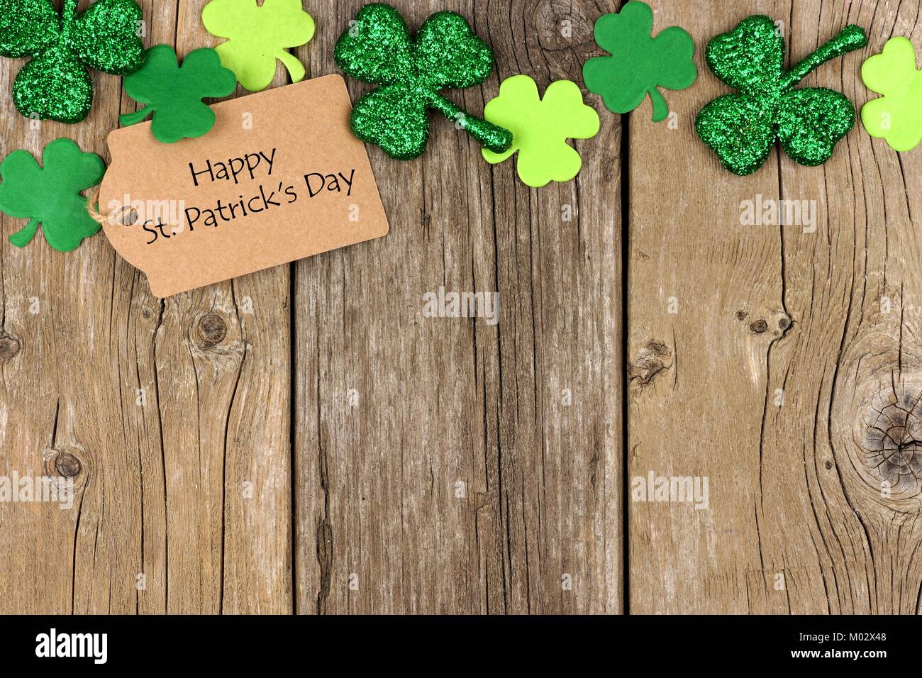 Happy St Patricks Day tag mit oberer Rand der glänzenden Shamrocks über eine rustikale Holz Hintergrund Stockfoto