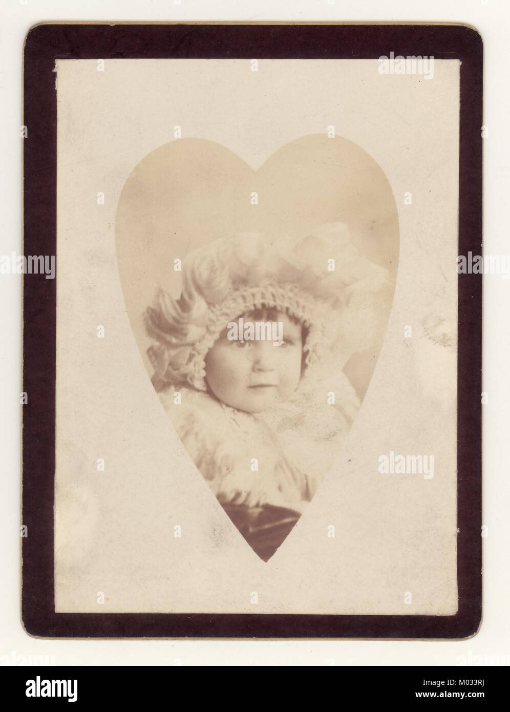 Studio-Porträtfoto in Herz-Vignette von niedlichen Baby Junge oder Mädchen in aufwendigen Haube um 1890er. Die Karte ist schwarz, so dass dies eine Gedenkkarte für ein verstorbenes Kleinkind sein könnte., Großbritannien Stockfoto